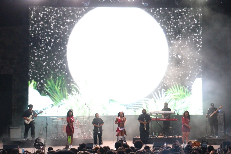 wide shot of screen on stage depicting large white circle and leaves, victoria monet, dancers, and band on stage