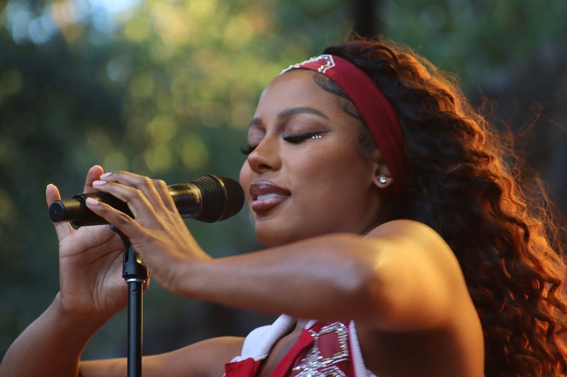 close up shot of victoria monet holding microphone with both hands, wearing stanford gear