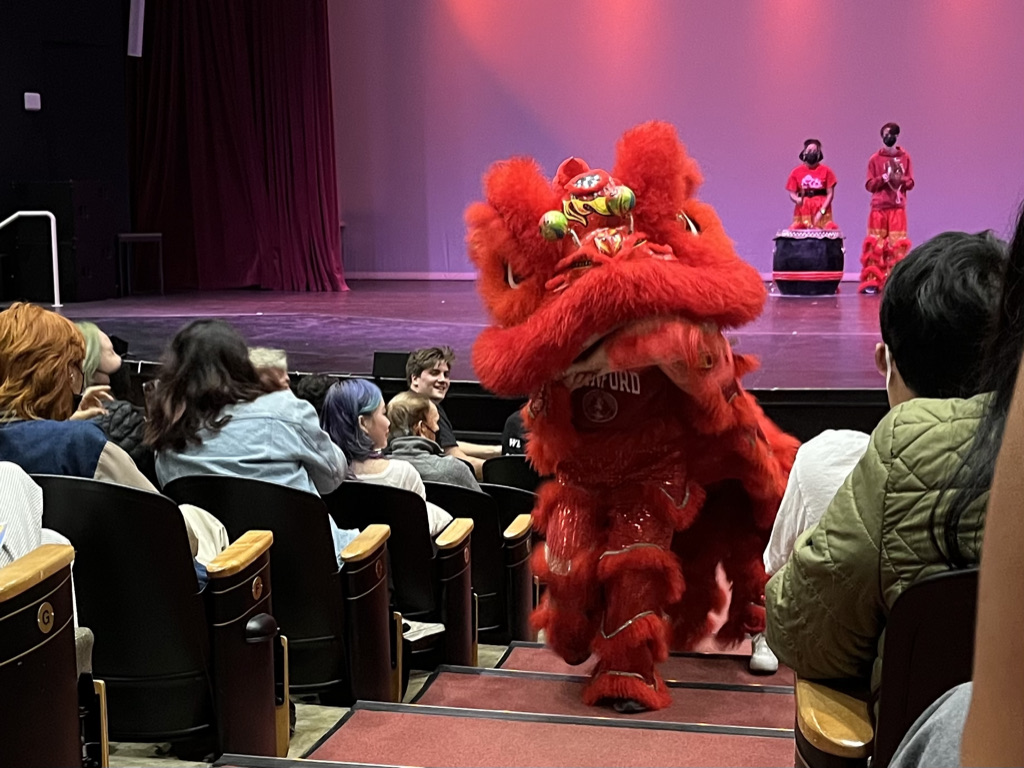 A life sized red lion puppet operated by two students walks up the aisle of Dinkelspiel Auditorium