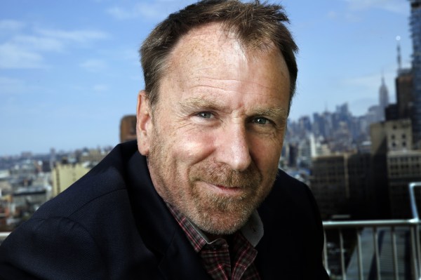 a welColin Quinn with trimmed beard smiles and looks directly at the viewer , with the New York skyline under a blue sky behind him