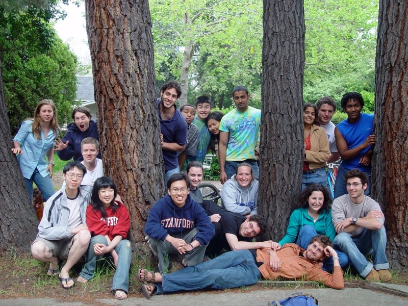 A group of students smile and pose outside, around three trees. 