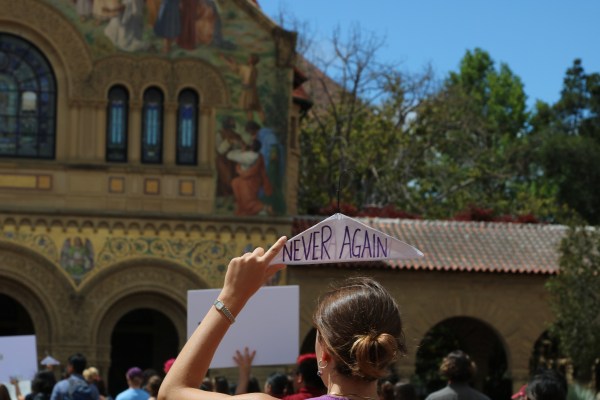 A woman holds a hanger that reads "never again" in front of Stanford Memorial Church