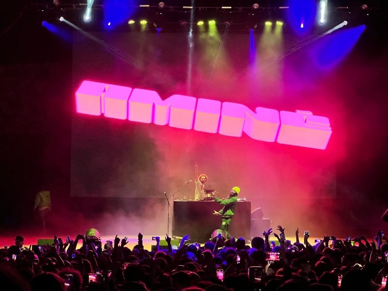 Amine performs in front of a screen with a 3D sign of him to a crowd