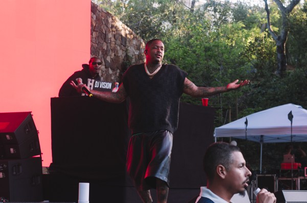 Blackfest headliner YG looks to the audience during his performance. He stands on stage with both of his hands up and with a grin on his face.
