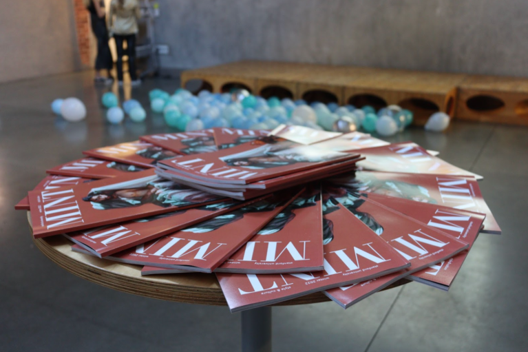 Copies of MINT sit stacked on a table with maroon covers.