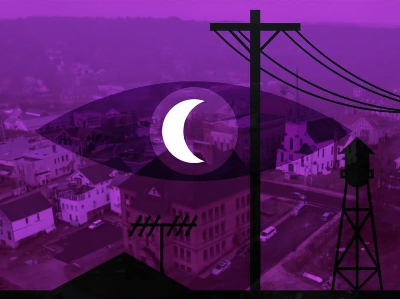 A creepy town overlayed by the shadow of an eye with a crescent moon in its iris, and overhead wires extending into the night.