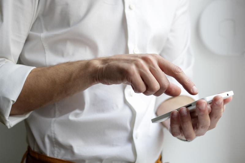 a person wearing a dress shirt with their right hand hovered above a smartphone, which is held in their left hand