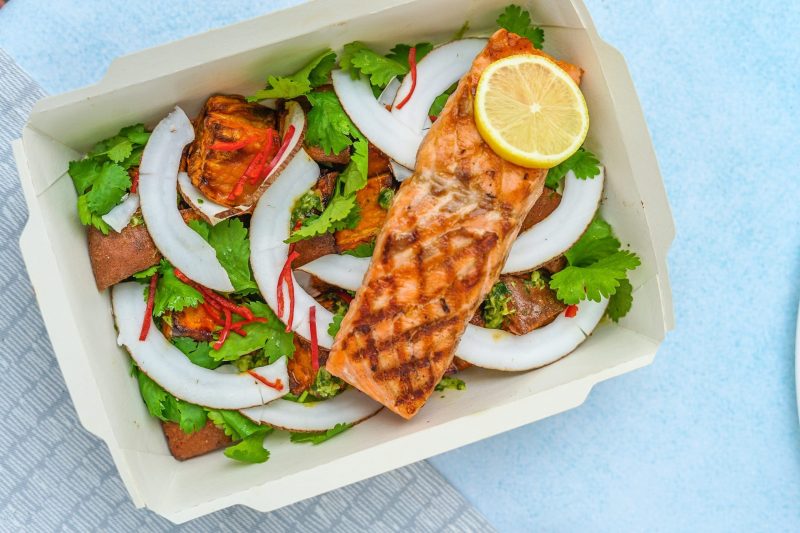 a food take-out box with salmon and a slice of lemon on a bed of