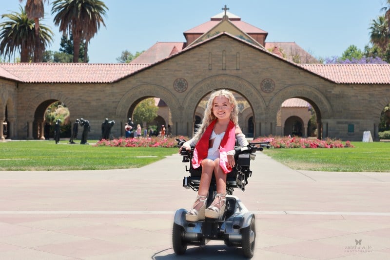 Tilly sits in front of main quad in a white dress and red stoll