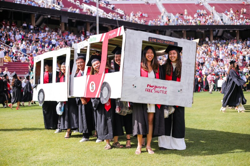 A dozen graduates perform the "Wacky Walk" with a cardboard version of the Marguerite Shuttle.
