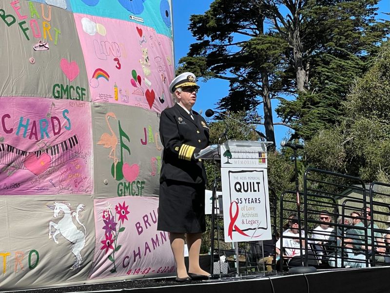 Levine gives a speech from a stage. A sign on her podium reads "THE AIDS MEMORIAL QUILT 35 YEARS of Love Activism & Legacy"