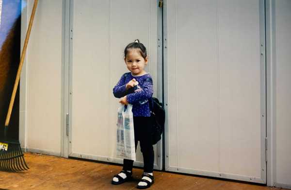 A child stands carrying a plastic bag containing a newspaper.