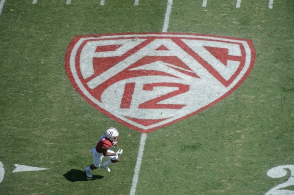 An aerial view of a football field with the Pac-12 logo as a Stanford football player runs near the bottom of the logo.