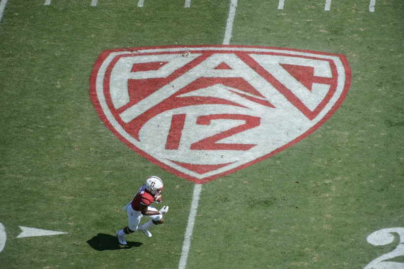 An aerial view of a football field with the Pac-12 logo as a Stanford football player runs near the bottom of the logo.