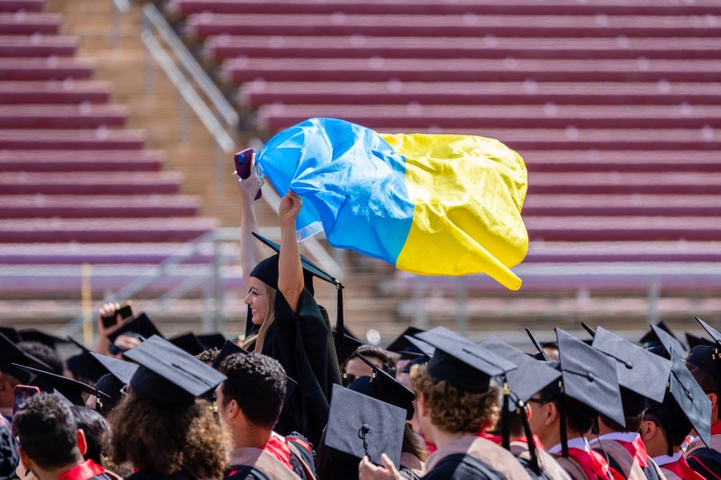 A student waves the blue and yellow Ukrainian flag above a sea of graduation caps