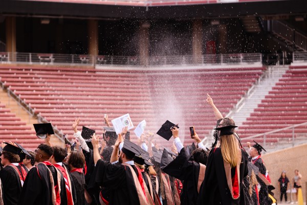Graduates wearing caps and gowns stand and cheer in the audience of Stanford's 2022 commencement ceremony at Stanford stadium