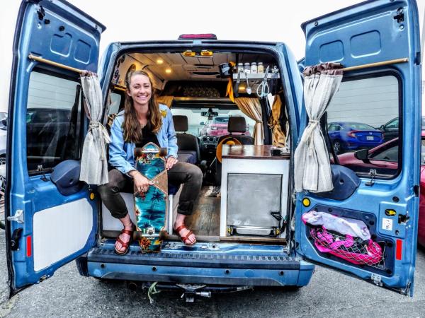 Huemer sits in the back of her van with numerous possessions and equipment for the road, smiling