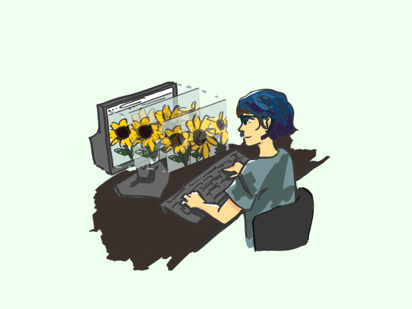 A woman sits at a computer looking at a photo of sunflowers.