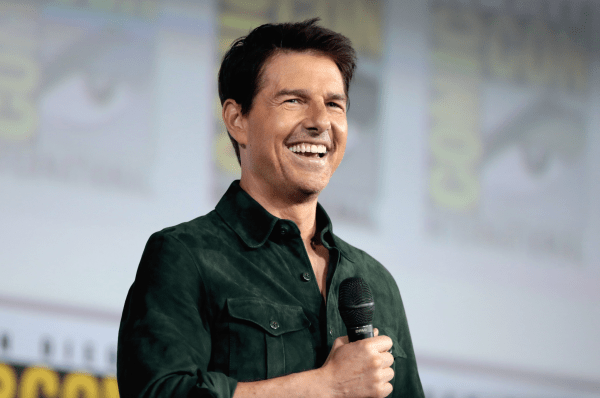 Tom Cruise smiling in a green shirt and holding a mic as he speaks at the 2019 San Diego Comic Con International, for "Top Gun: Maverick", at the San Diego Convention Center in San Diego, California.