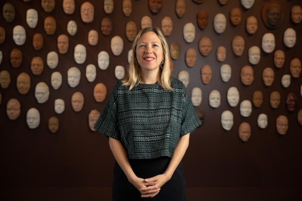 Veronica Roberts smiles in front of a wall of face sculptures.