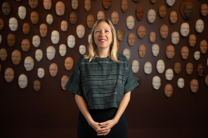 Veronica Roberts smiles in front of a wall of face sculptures.