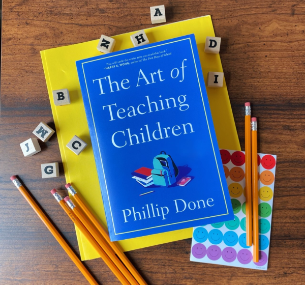 Blue book cover with text: "The Art of Teaching Children, Philip Done". The book is surrounded by stationery: pencils, stickers, scrabble tiles, and a folder.