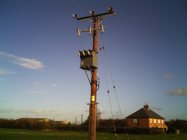 Electricity transformer in a grass field in front of a brick house