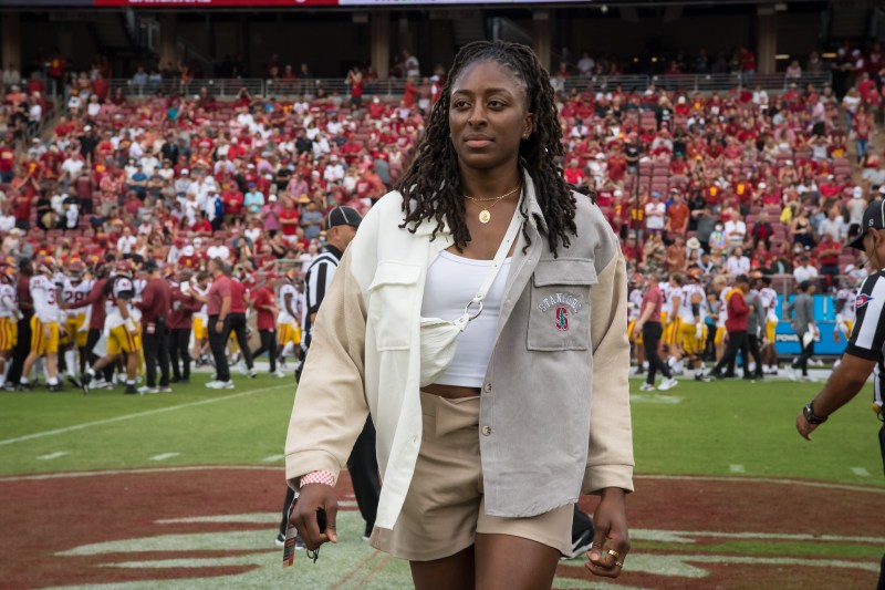 A woman stands in front of the Stanford Stadium crowd.