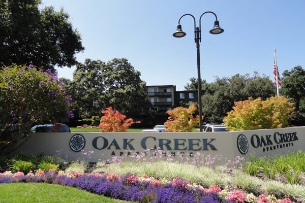 A garden in front of a short building and sign that reads "Oak Creek Apartments"