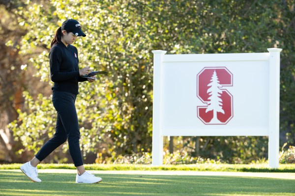 A women's golfer walks by a board with the Stanford logo.