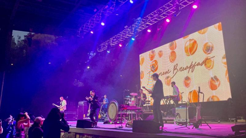 Japanese Breakfast performing on stage with their band name and persimmons shows on the big screen