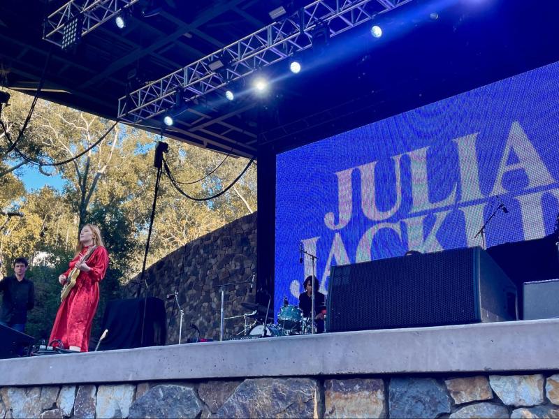 Julia Jacklin playing the guitar onstage with the text "JULIA JACKLIN" displayed on the big screen behind her