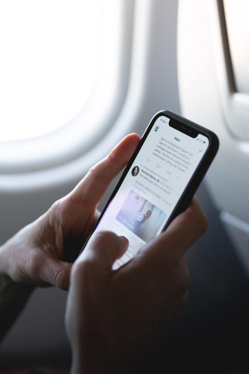 A woman seated by a plane window scrolls through Twitter on an iPhone.