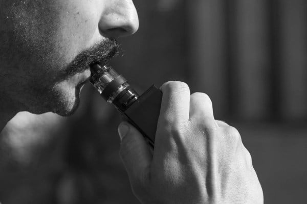 Black and white closeup of a man with a vape in his mouth