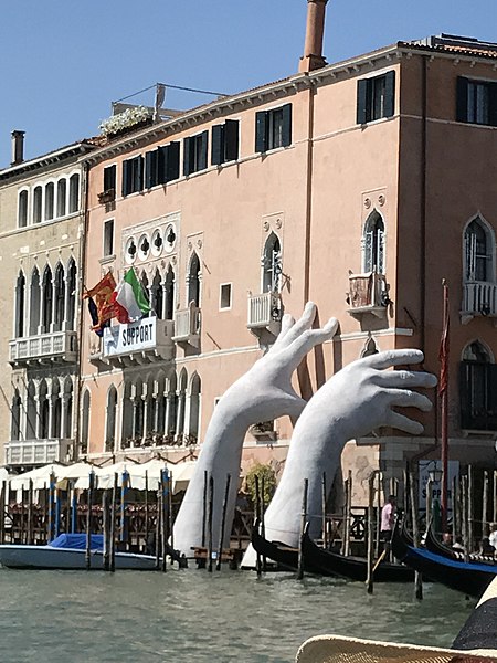 Two plaster hands extending out of the water touch the buildings near by