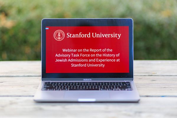 Laptop positioned on outdoor table with red screen reading "Webinar on the Report of the Advisory Task Force on the History of Jewish Admissions and Experience at Stanford University.)