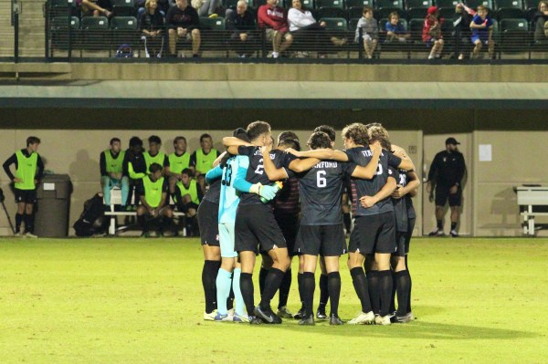 the men's soccer team huddles on the pitch