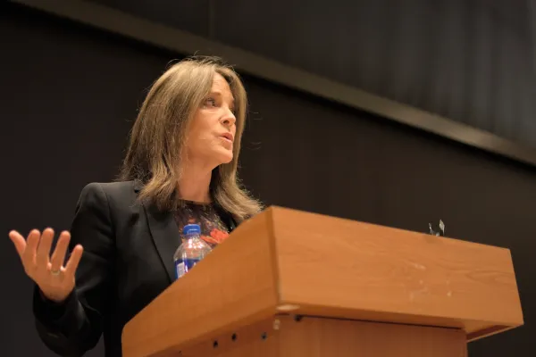 Lower side view of Marianne Williamson with arms spread at a podium
