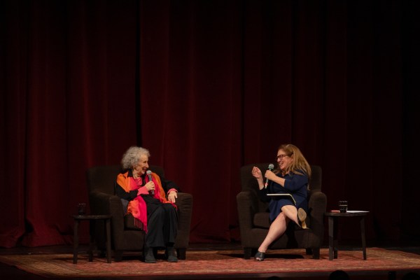 Margret Atwood and Dahlia Lithwick on stage as they face each other sitting on chairs with mics in their hands, laughing together.