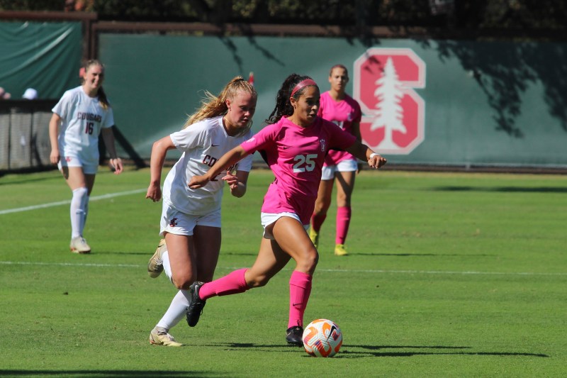 Stanford player with jersey number 25 prepares to kick the ball while running, closely followed by a Washington State player