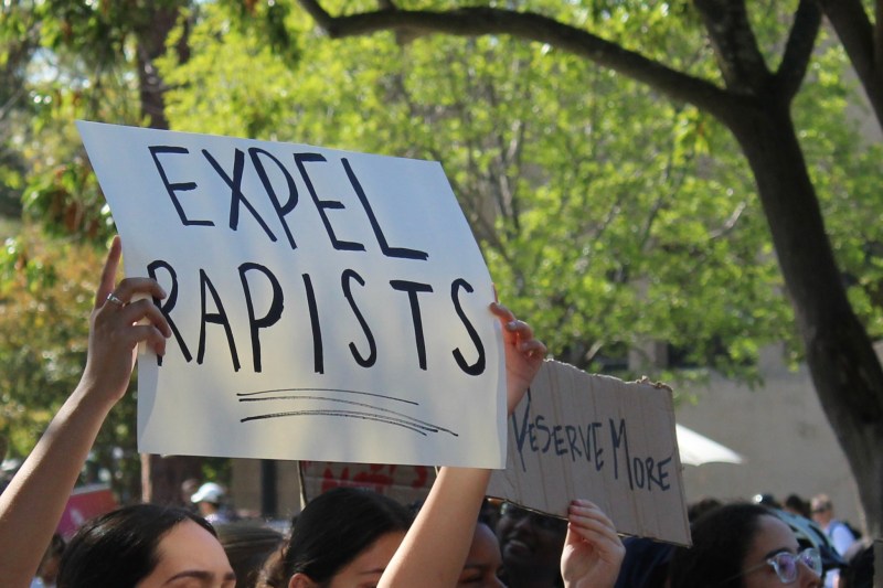 A protester holds up a sign that reads "EXPEL RAPISTS" during a protest held by Sexual Violence Free Stanford on Friday afternoon
