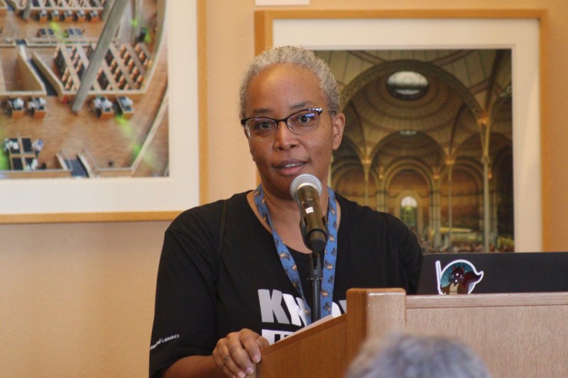 Felicia Smith at a podium with a microphone, talking and looking at camera.