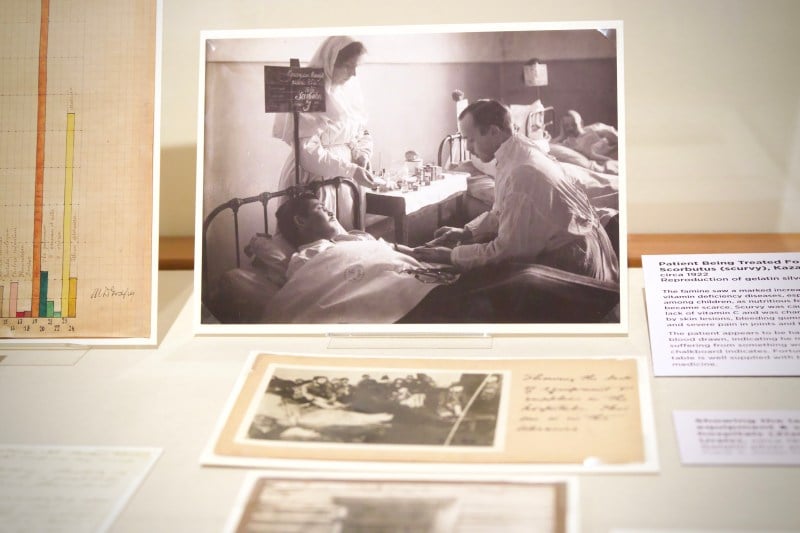 A black and white photograph of a doctor diagnosing a bedridden patient