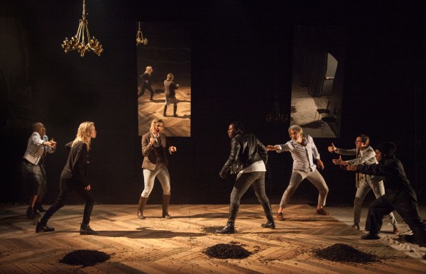 On a darkened stage, seven actors stand facing each other in a visible conflict