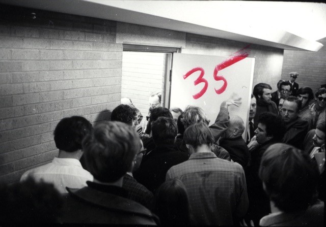 Black and white image of Stanford students in the 60s jostling against each other, including the writer Lenny Siegel and Fred Glover.