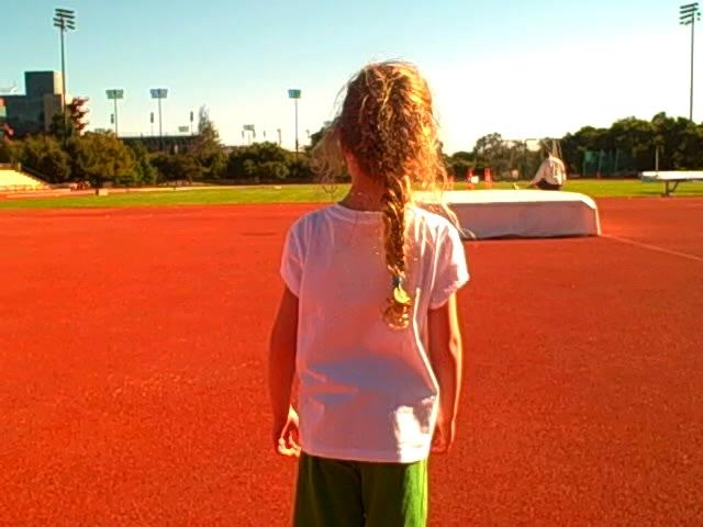 A young girl stands on a track and looks at a football in the