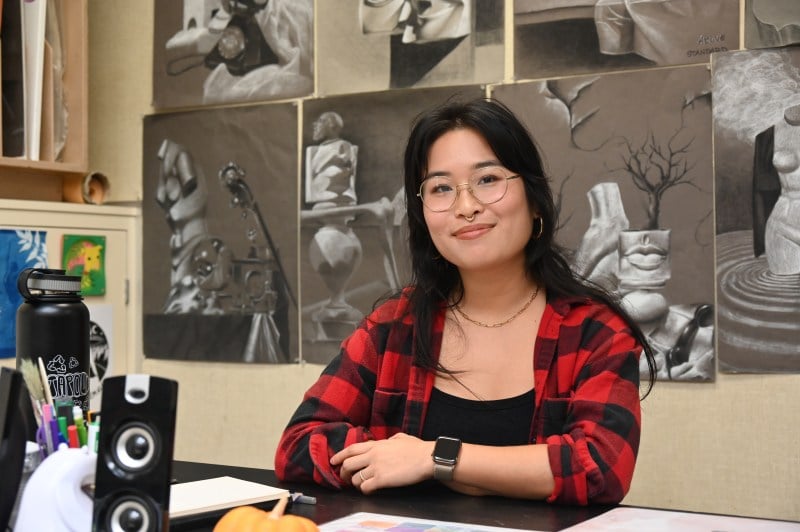 Anita Su sits in front of student artwork.