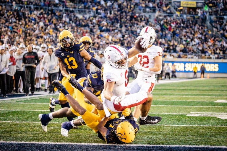 A football player extends into the end zone with an opponent under him