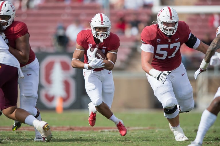 A football player in a red uniform and white football player runs behind his teammate