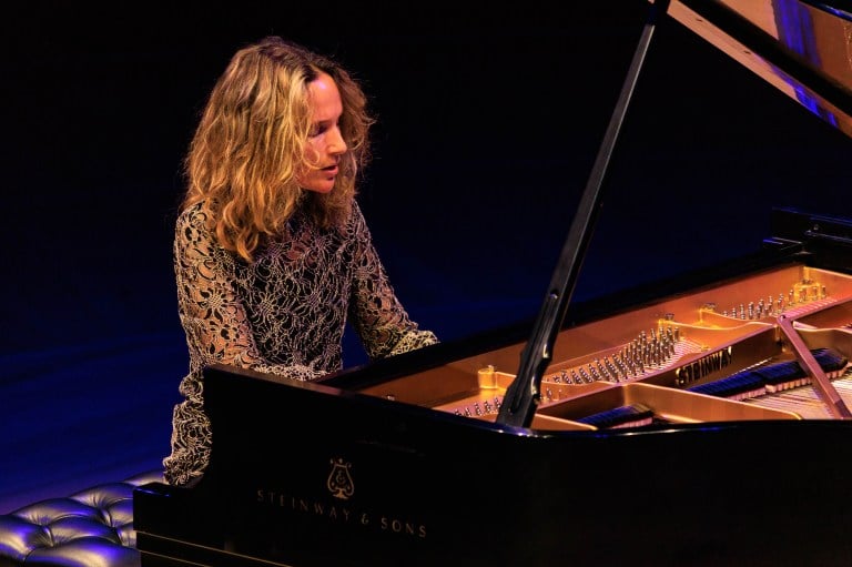 A photo of a woman sitting at the piano and playing it with soft light shining on her.